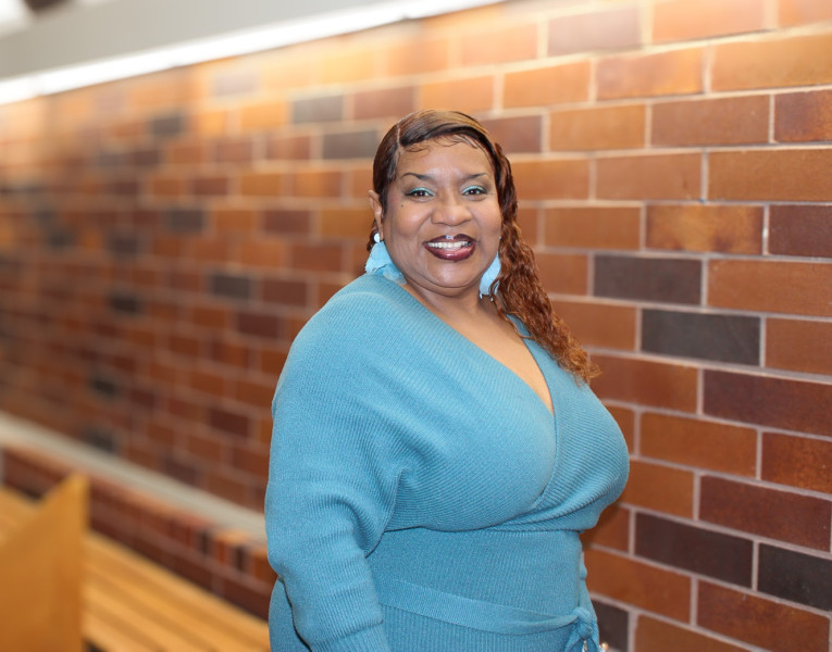 A smiling woman in a blue dress standing in the entry atrium of Governors State University