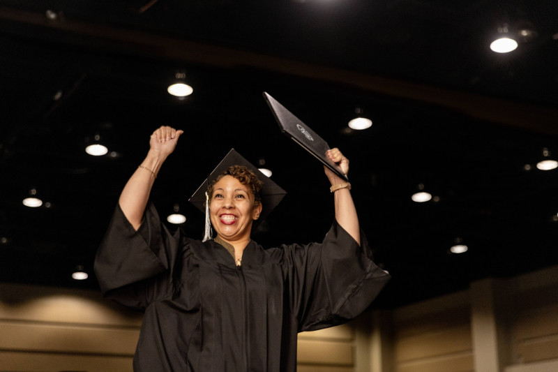 A graduate raising her hands in the air while holding her diploma