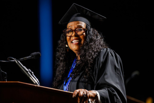 A woman Catharine Miles in academic regalia speaking at a podium for Governors State University 2025 Commencment