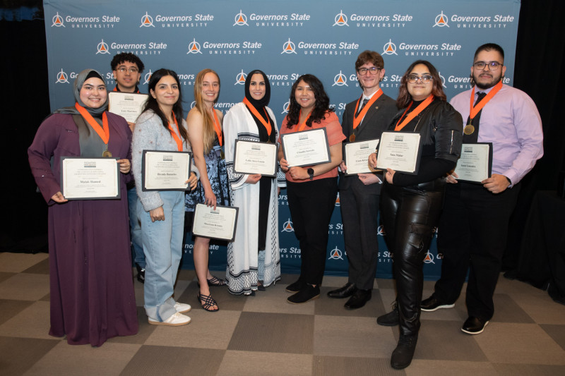 Nine Governors State University students wearing honors medallions and holding framed certificates