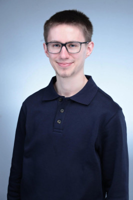 Professional headshot of a smiling man wearing a black long sleeve shirt and glasses