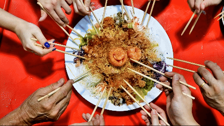 Close-up of people tossing yusheng or yee sang during Chinese New Year dinner celebration for good luck