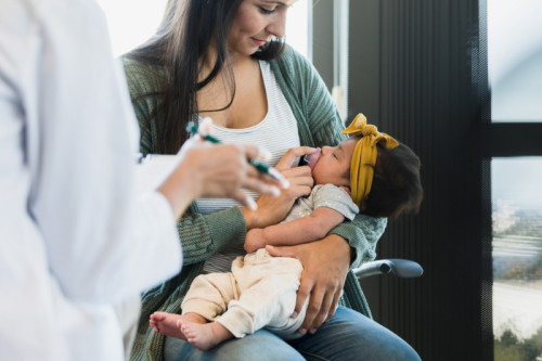 Young mother takes her baby in for a routine checkup. She puts a pacifier in the sleepy baby's mouth as the unrecognizable person explains something.
