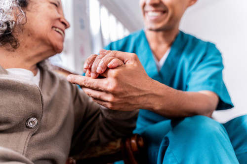 Senior woman holding caregiver&#039;s hands at home