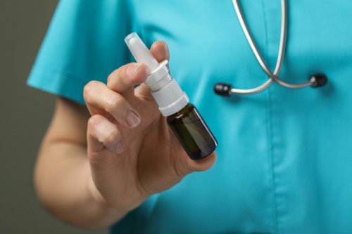Woman holding nalaxone nasal spray bottle on olive background, closeup,