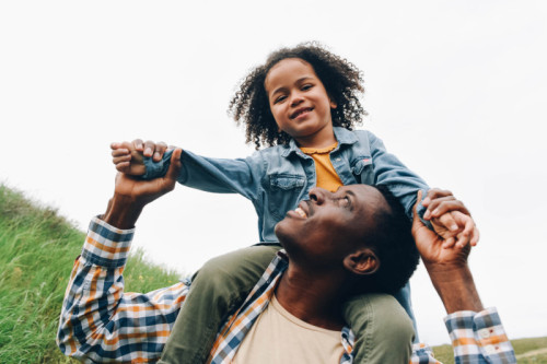 Black dad and daughter are having fun. A little girl sits on dad's shoulders.