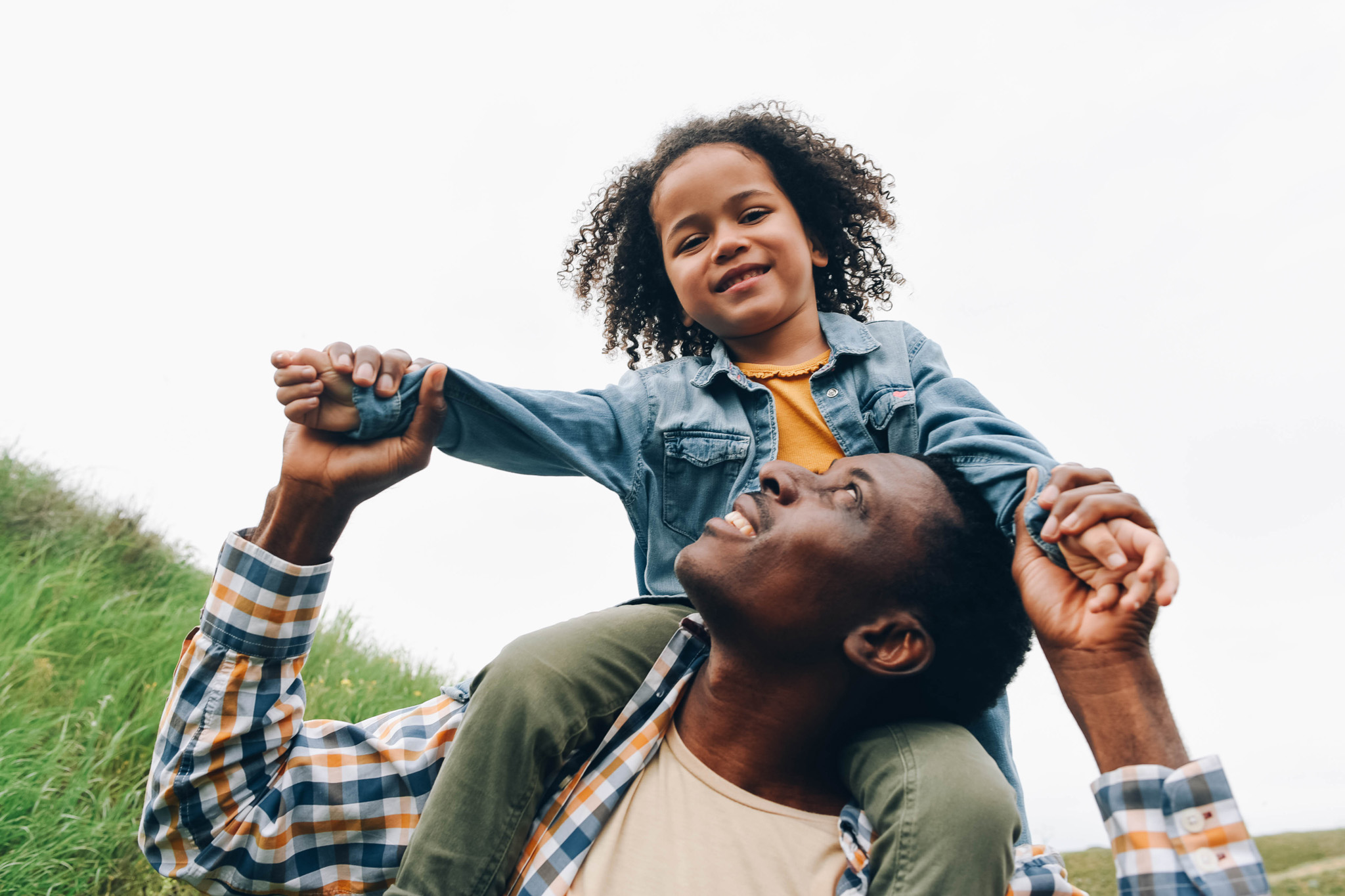 Black dad and daughter are having fun. A little girl sits on dad's shoulders.