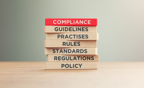 Compliance related words written wood blocks sitting on a wood surface in front of a defocused background. Compliance concept.