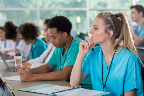 Attentive Caucasian female nursing student listens to professor&#039;s lecture.