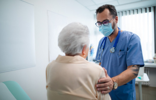 Mid-adult doctor with elderly patient in examination room in clinic, coronavirus concept.