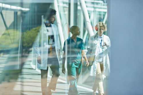 Multiracial medical workers discussing while walking on elevated walkway seen through glass