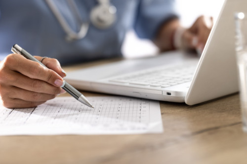 The doctor analyzes the patient&#039;s EKG chart and accurately analyzes the medical report and records it in the internet database using a laptop.