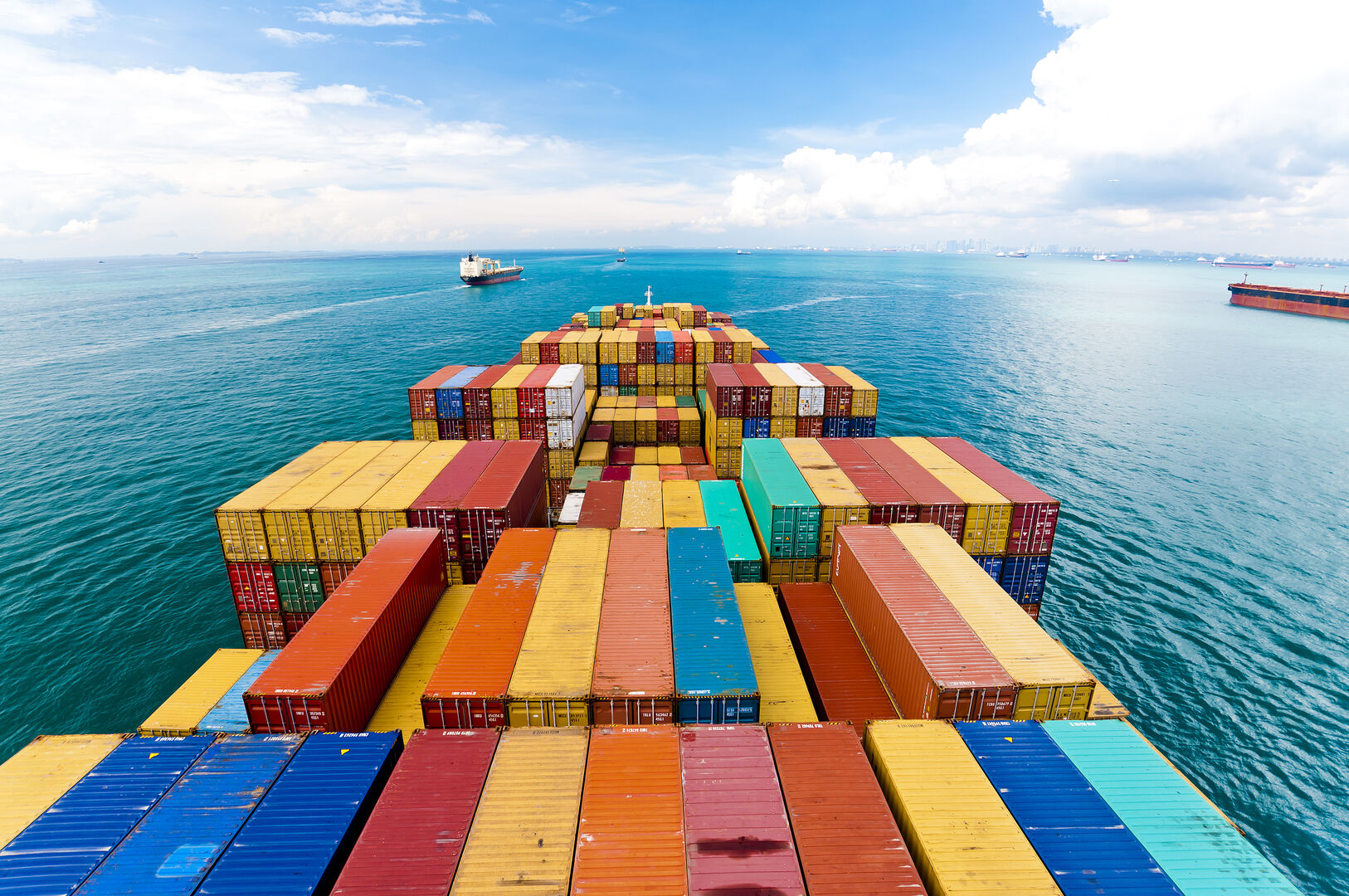Container ship carrying stacked cargo containers sailing across the ocean under a blue sky