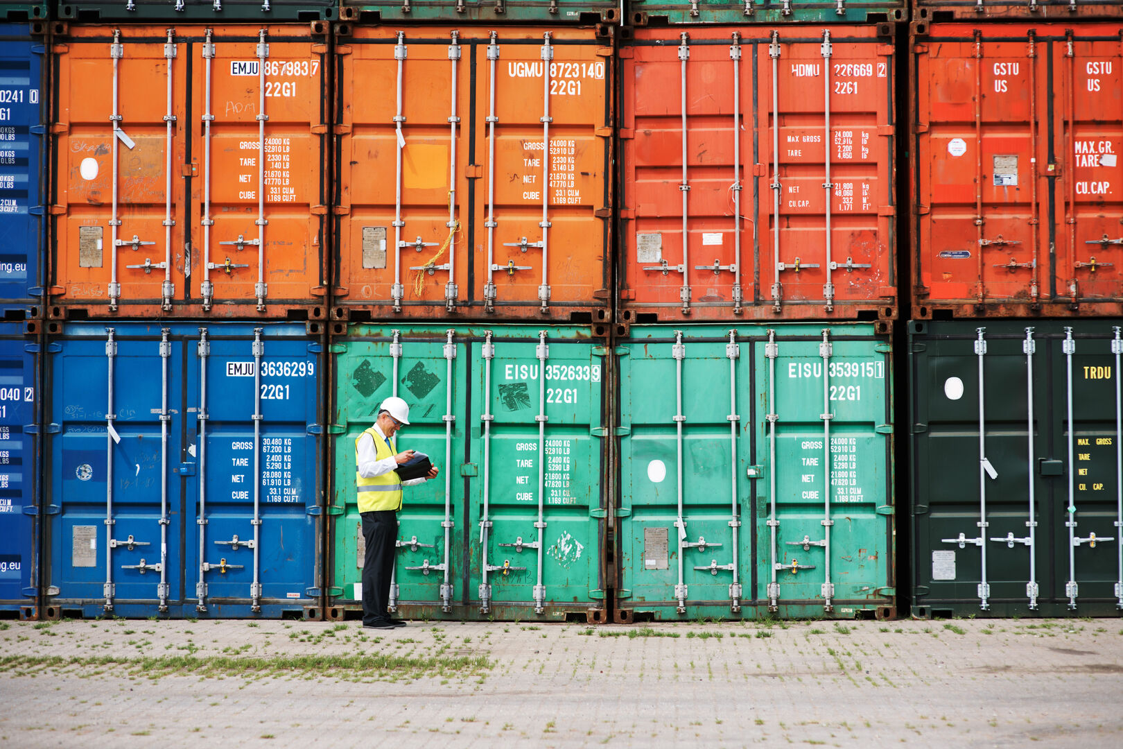 Logistics worker inspecting shipping containers and reviewing shipment data in a container yard
