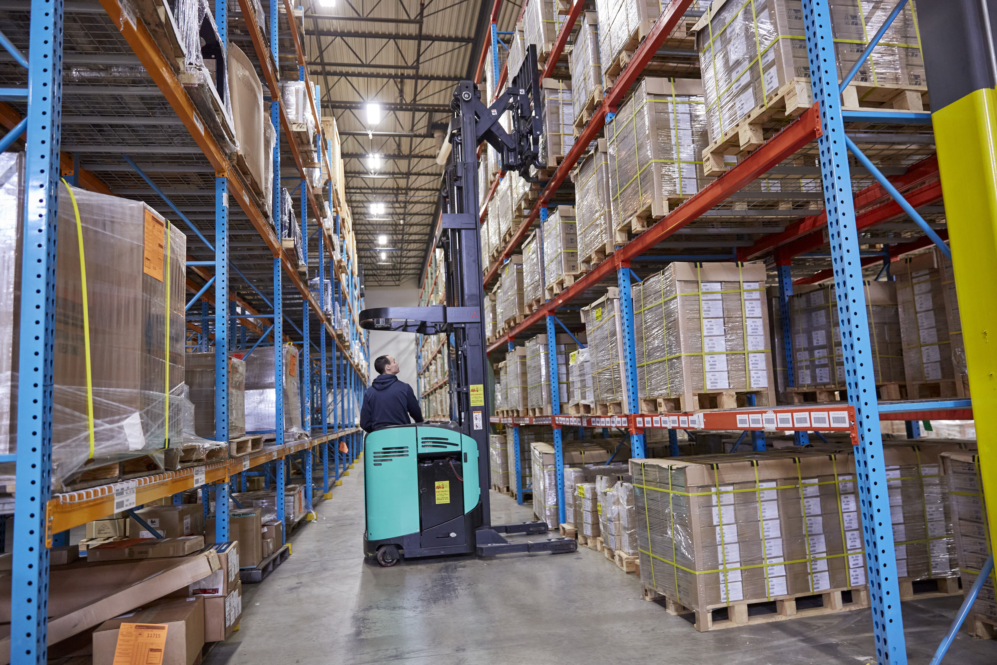 Forklift operator moving pallets in a logistics warehouse, showing 3PL fulfillment and supply chain storage operations.