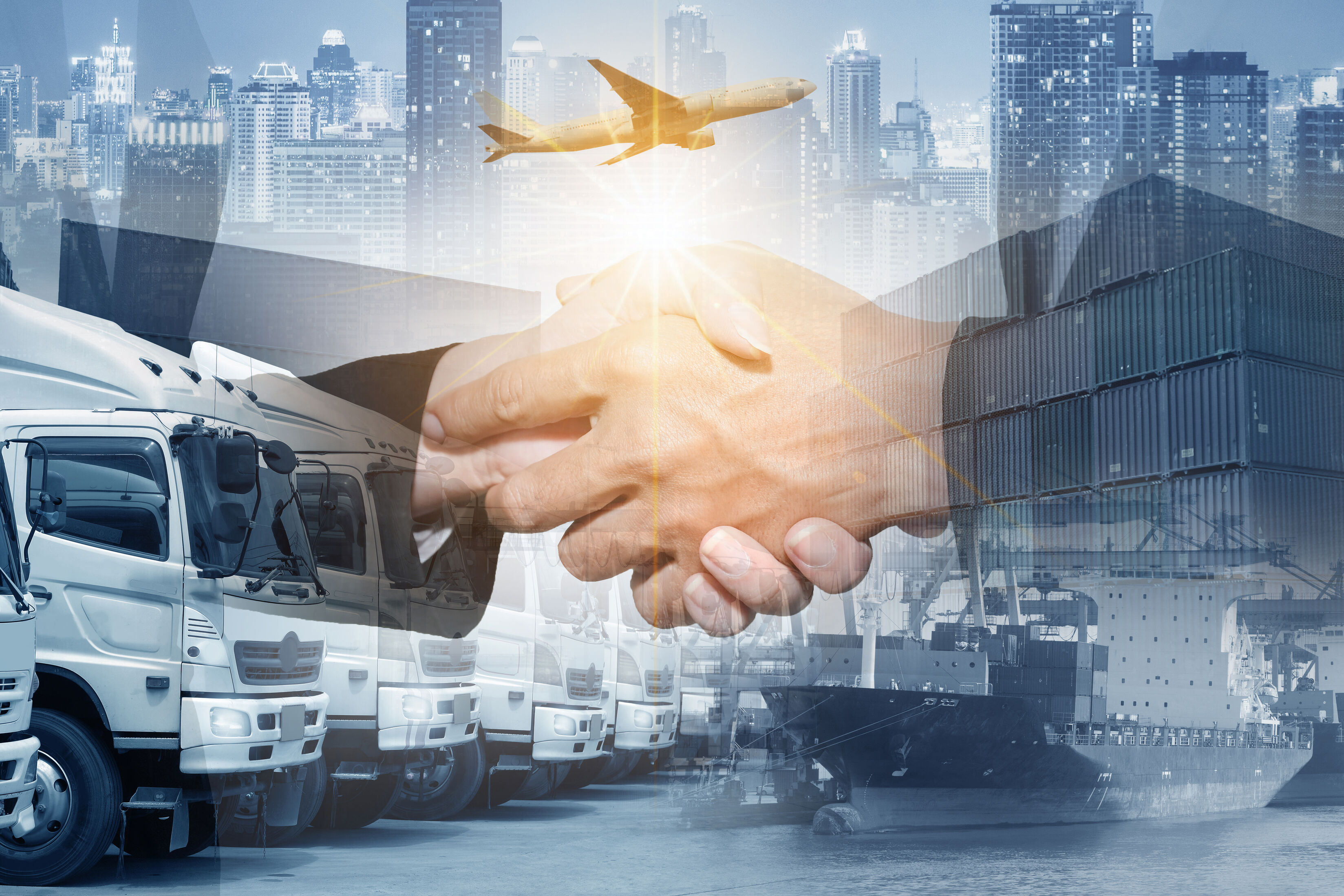 Business professionals shake hands over a global logistics background with trucks, containers and an aircraft.